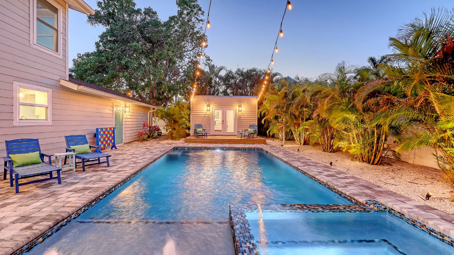 The pool and lit guest house under string lights at twilight